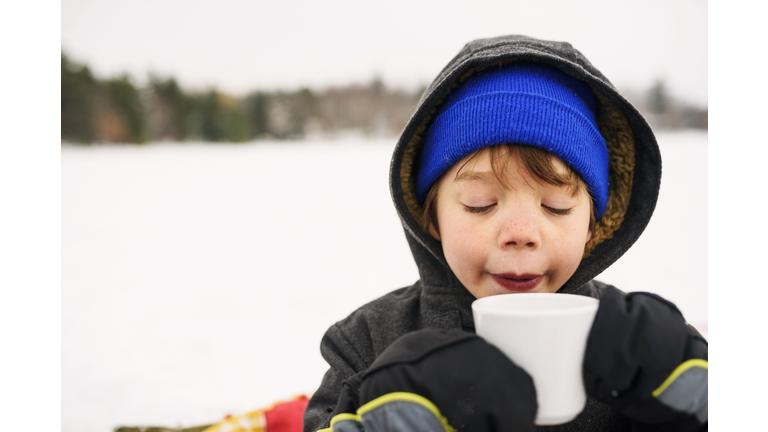 Boy standing in the snow drinking hot chocolate