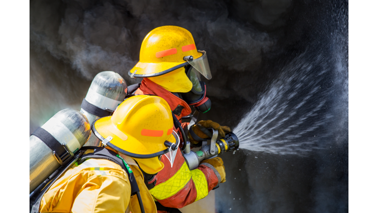 two firefighters water spray by high pressure nozzle to fire surround with smoke and copy space