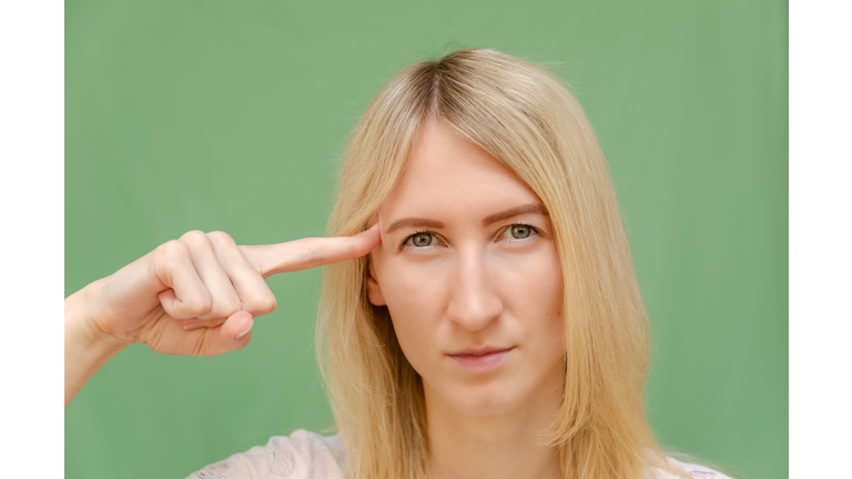 girl blonde on a green background holds a finger to his temple