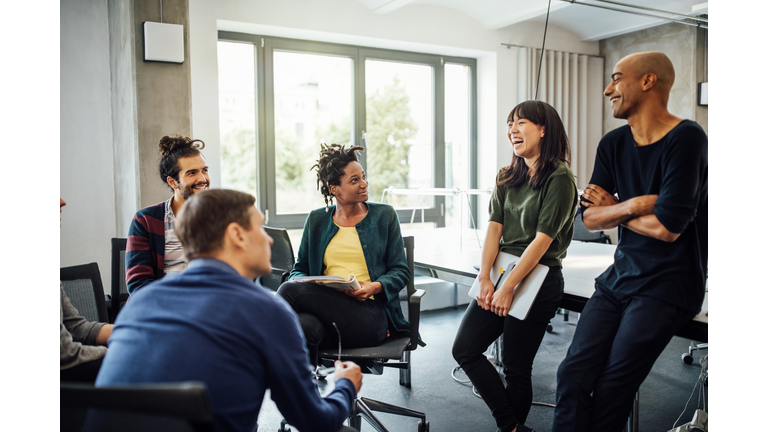 Colleagues looking at cheerful businesswoman in meeting