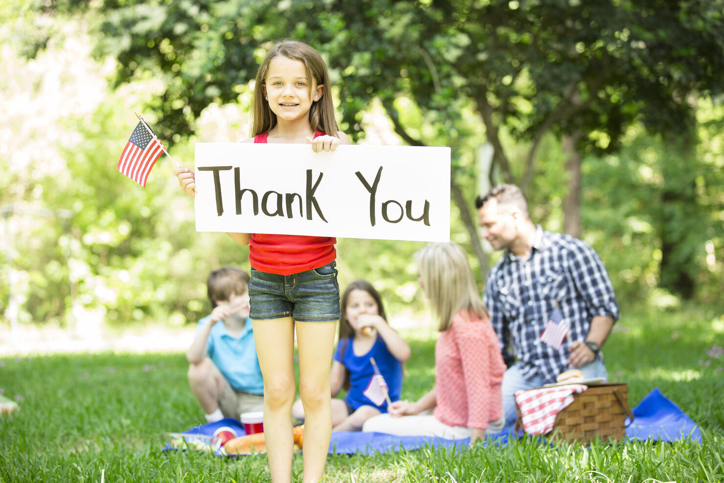 Child holds "Thank You" sign with American flag. Memorial Day.