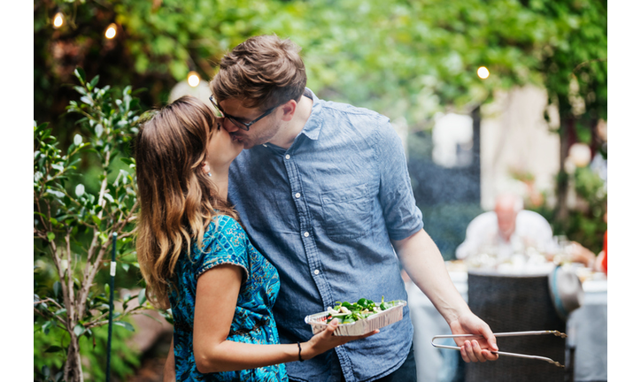 Couple Kissing While Cooking At Family BBQ