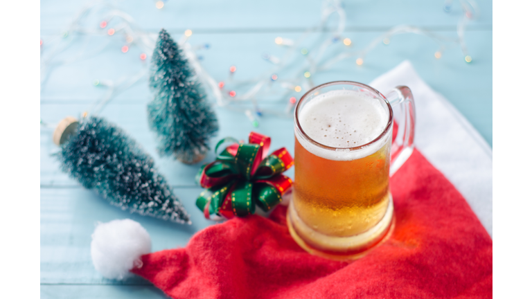 Glass of beer on christmas background with christmas tree, ribbon, santa claus hat and lights.