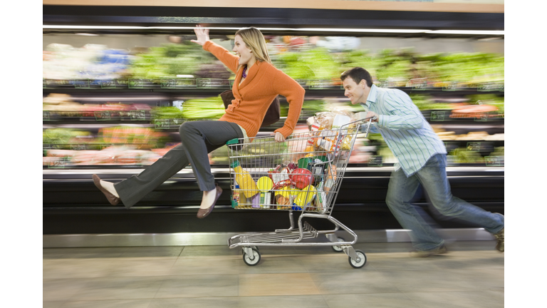 Man pushing woman in supermarket trolley down aisle, blurred motion