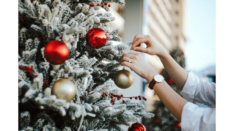 Cropped hand of woman decorating and hanging baubles on Christmas tree