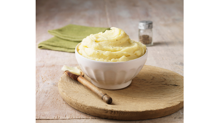 Ultimate mashed potato with black pepper in white faceted bowl with wooden spoon