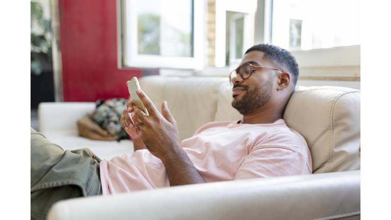 Relaxed man sitting on sofa using cell phone