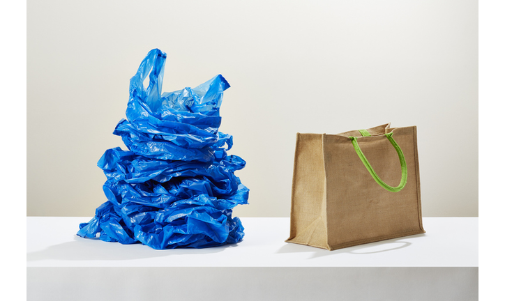A stack of plastic carrier bags next to a reusable shopping bag