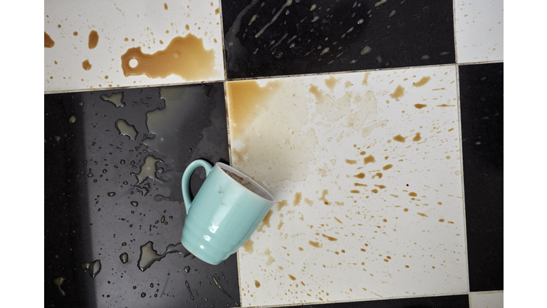 Cup on floor surrounded by spilt coffee, overhead view