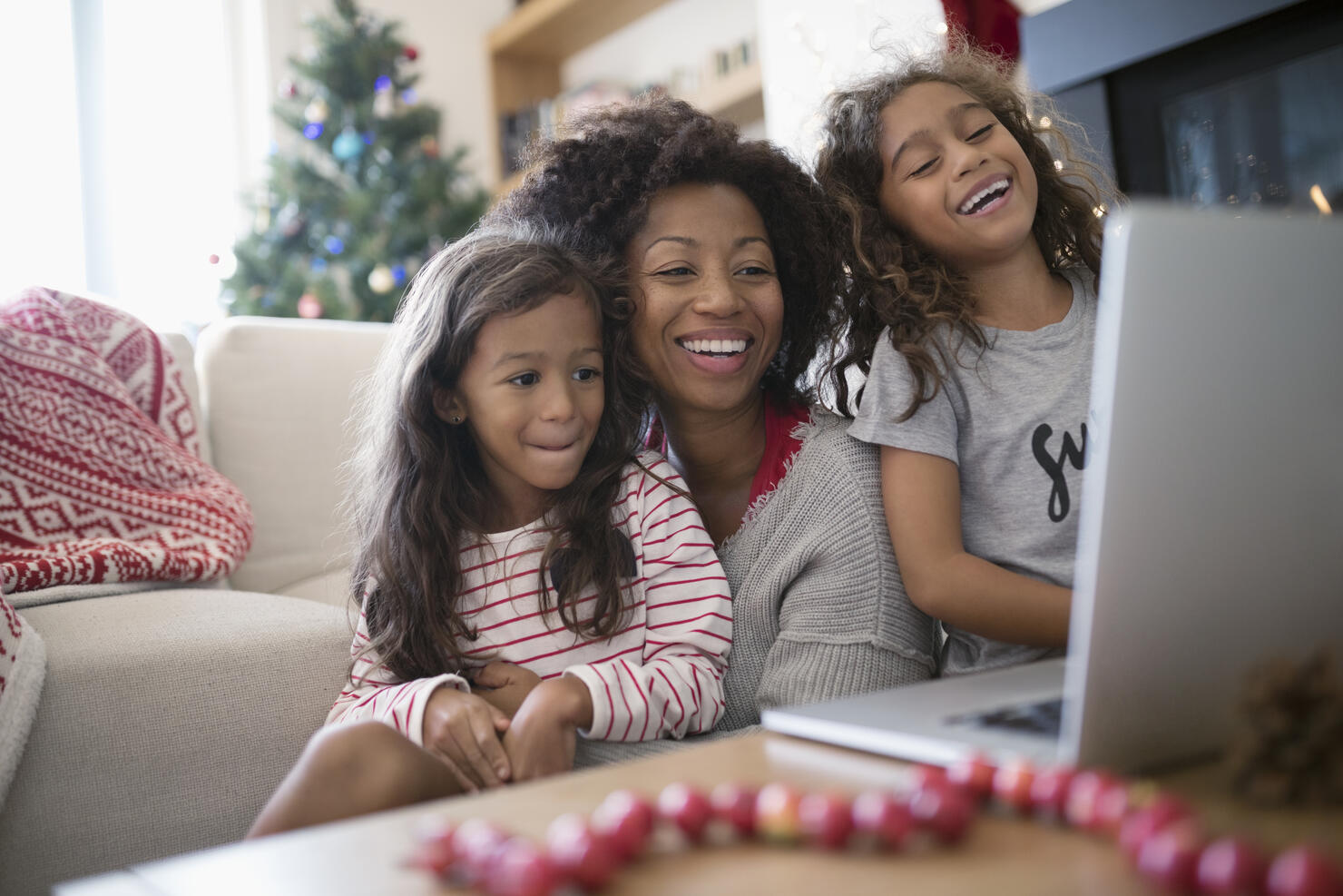 Laughing mother and daughters video chatting at laptop in Christmas living room