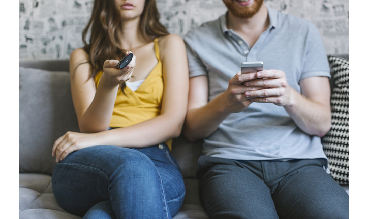 Couple sitting on couch with remote control and smartphone, partial view