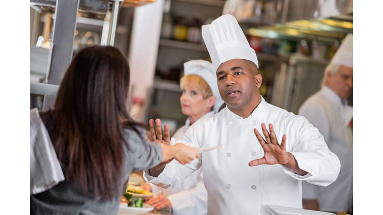 Restaurant manager yelling at chefs in kitchen with late tickets