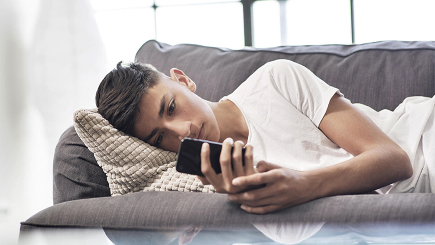 Teenage boy lying on sofa looking at smartphone