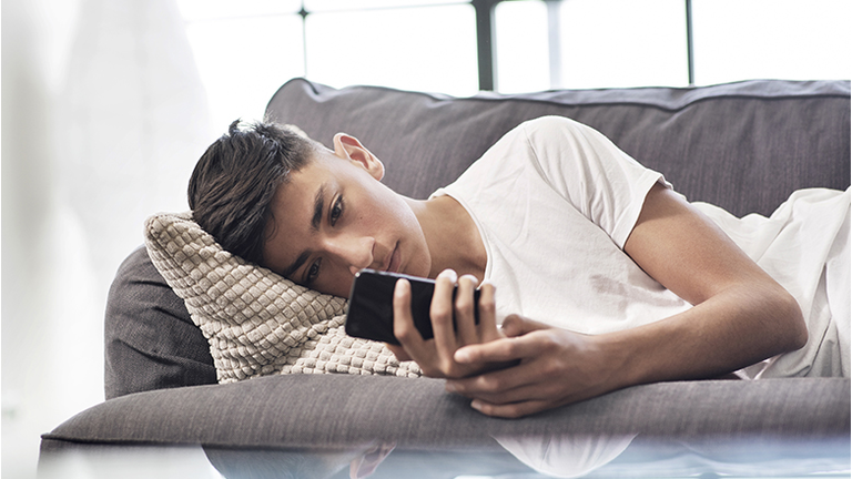 Teenage boy lying on sofa looking at smartphone