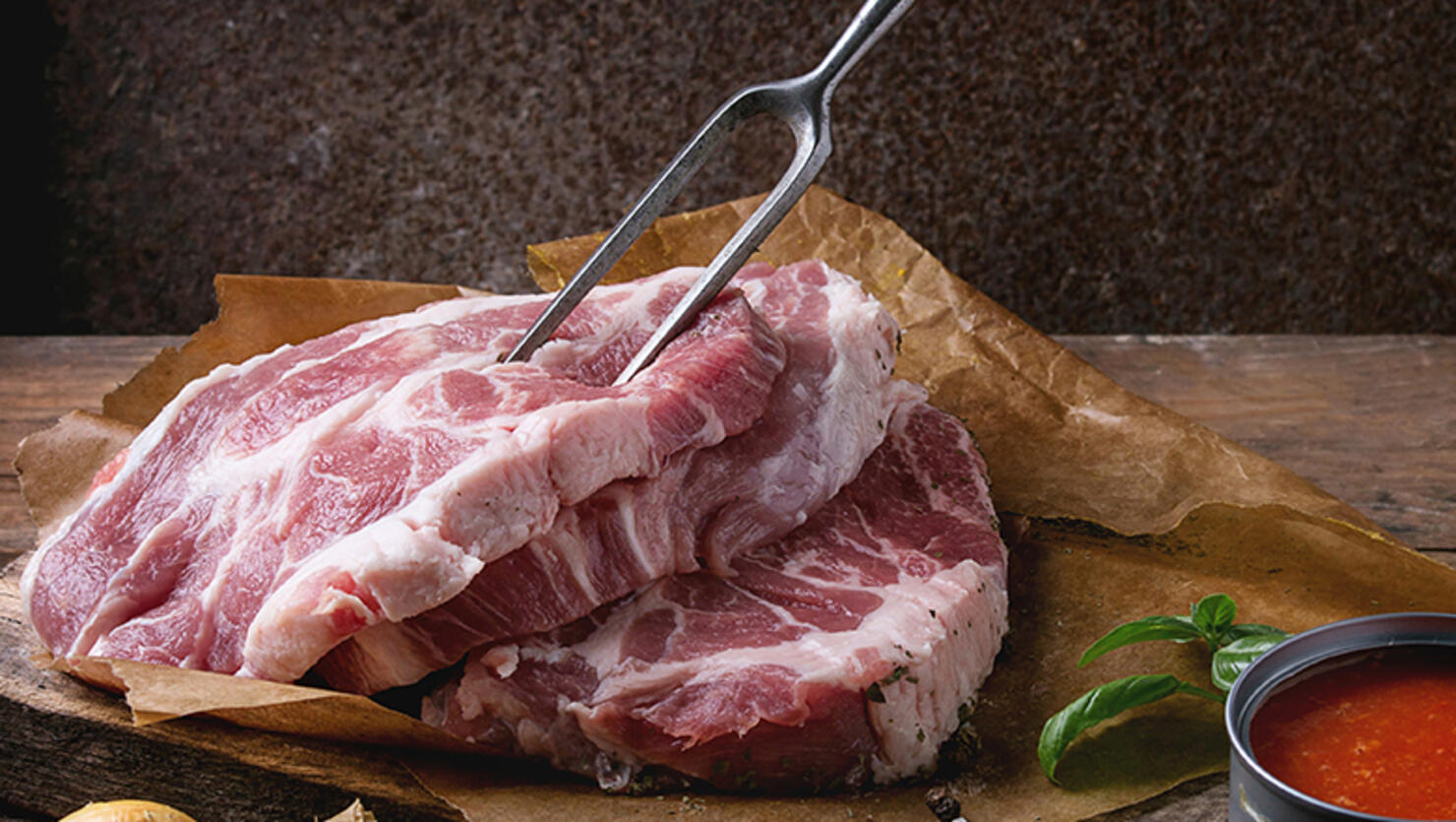 Raw steak meat pork neck on chopping board with shallot onion, tomato sauce marinade, basil and seasoning, served with meat fork over old wooden background. Dark rustic style. Square image