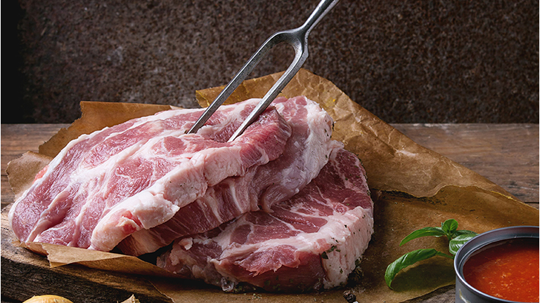 Raw steak meat pork neck on chopping board with shallot onion, tomato sauce marinade, basil and seasoning, served with meat fork over old wooden background. Dark rustic style. Square image