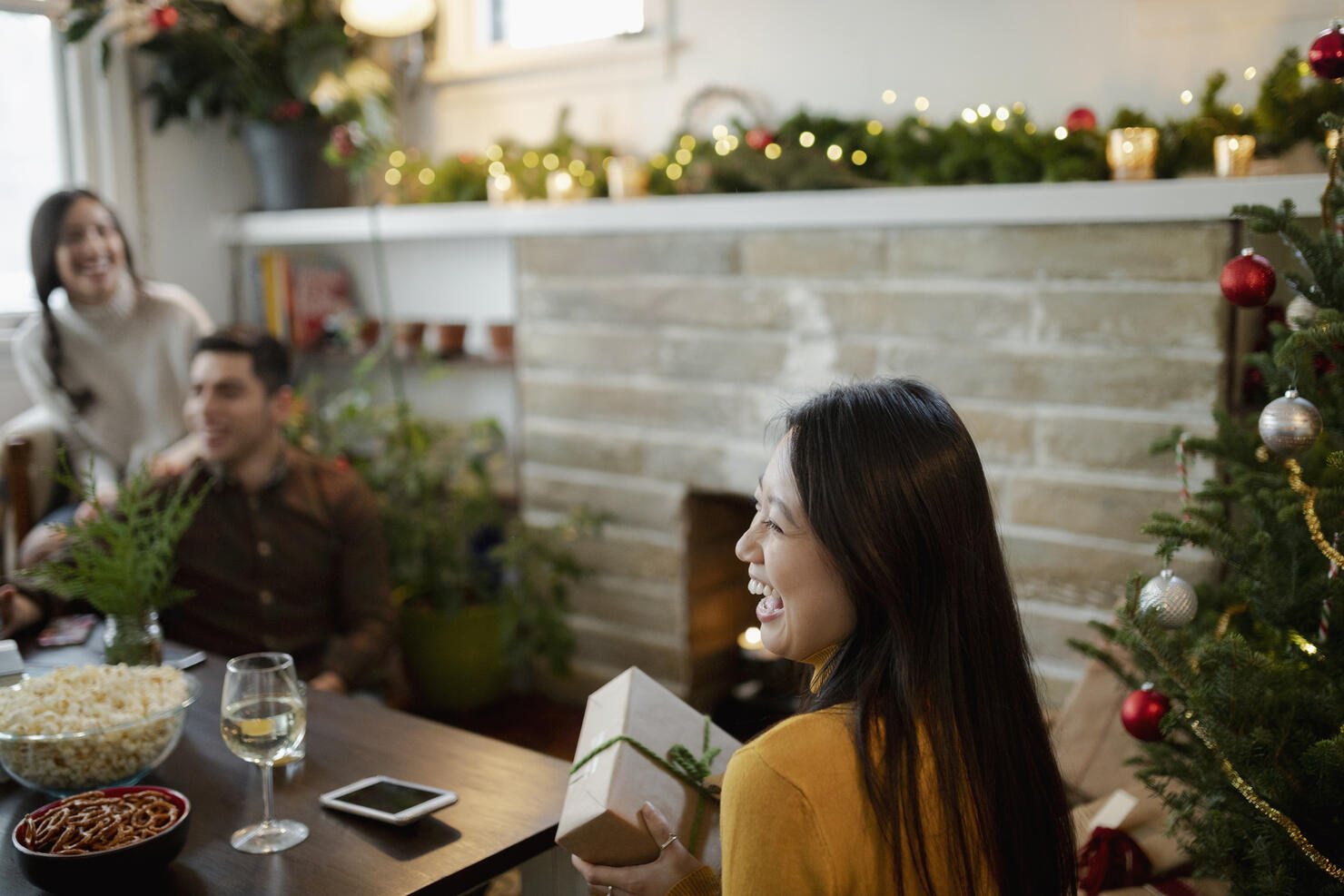 Happy young woman opening Christmas gifts with friends in living room