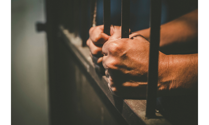 Cropped Hands Of Male Prisoner Holding Prison Bars