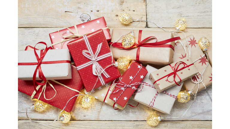 High angle view of a lot of wrapped Christmas gifts and strings lights on wooden background