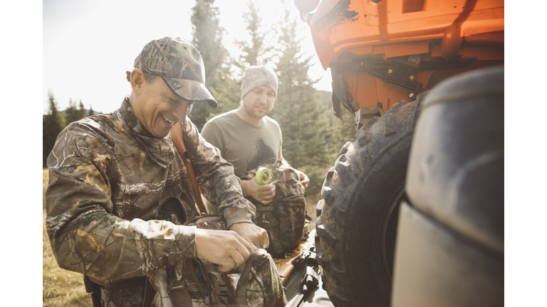 Father and son hunters preparing hunting equipment at quadbike