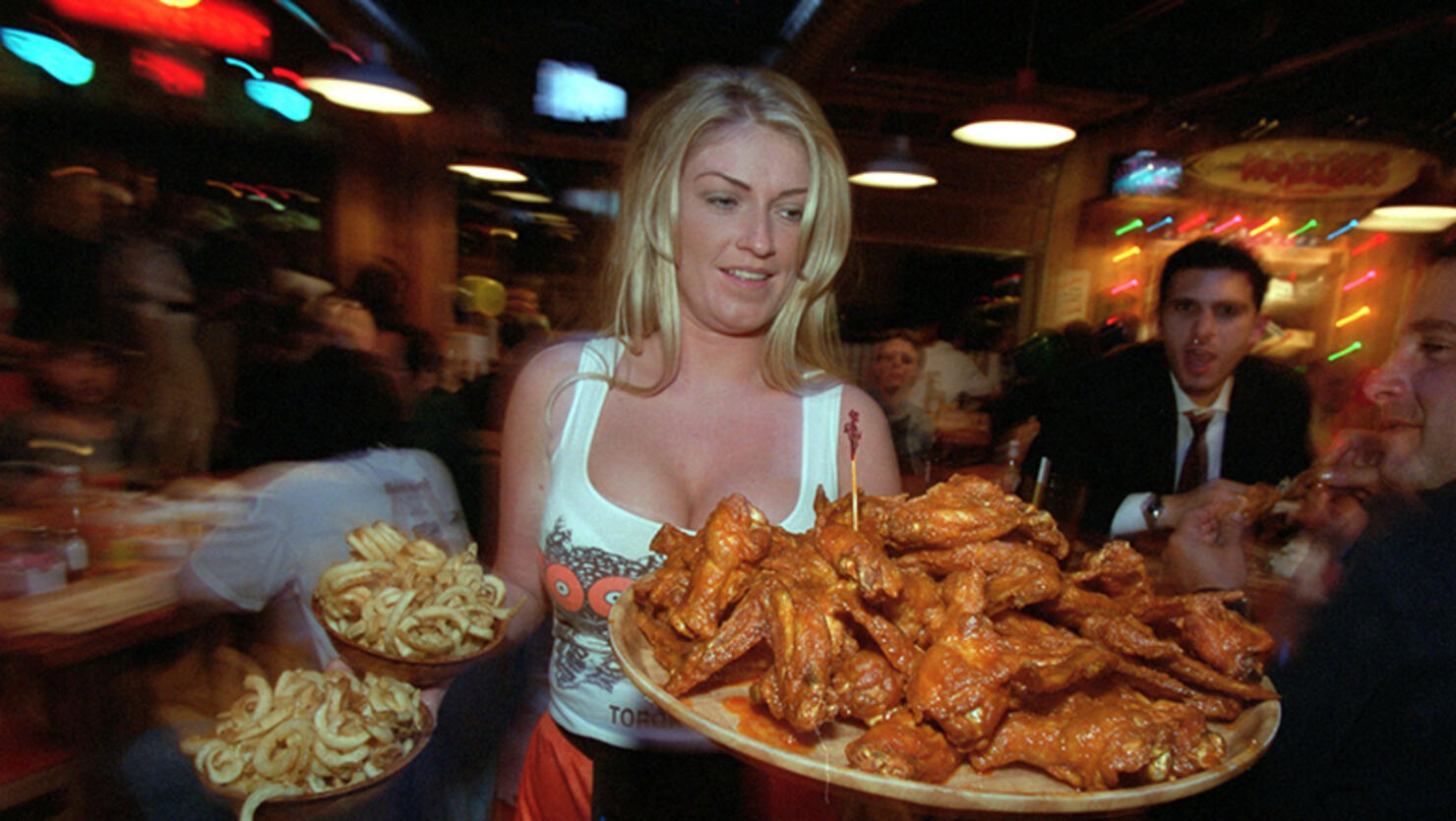 Marnie serves a burger, 2 shots, 3/4length and at table, Jules brings a large platter of wings, Sara