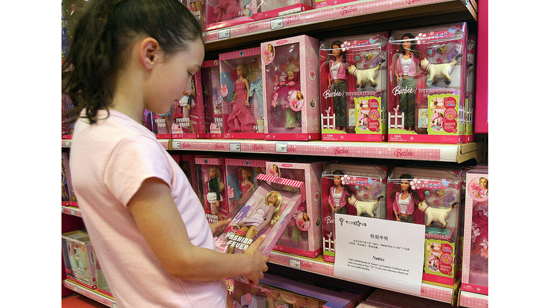 A young girl holds a Barbie doll next to