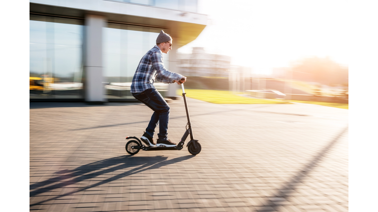 Side View Of Man Riding Push Scooter On Footpath
