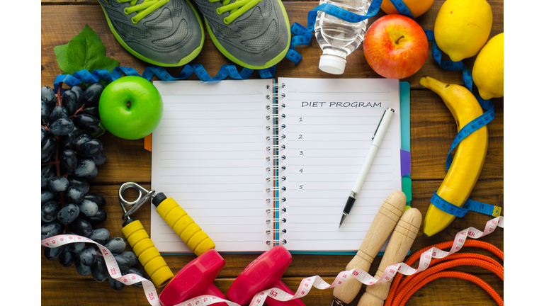 High Angle View Of Open Book Amidst Fruits And Exercise Equipment On Table