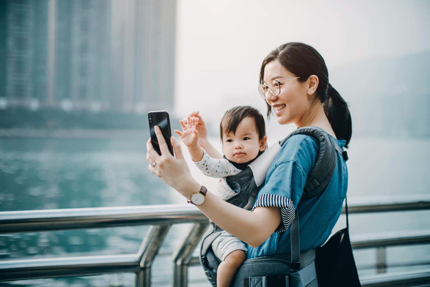 Mother and cute baby girl taking selfie joyfully with smartphone by the harbour in city