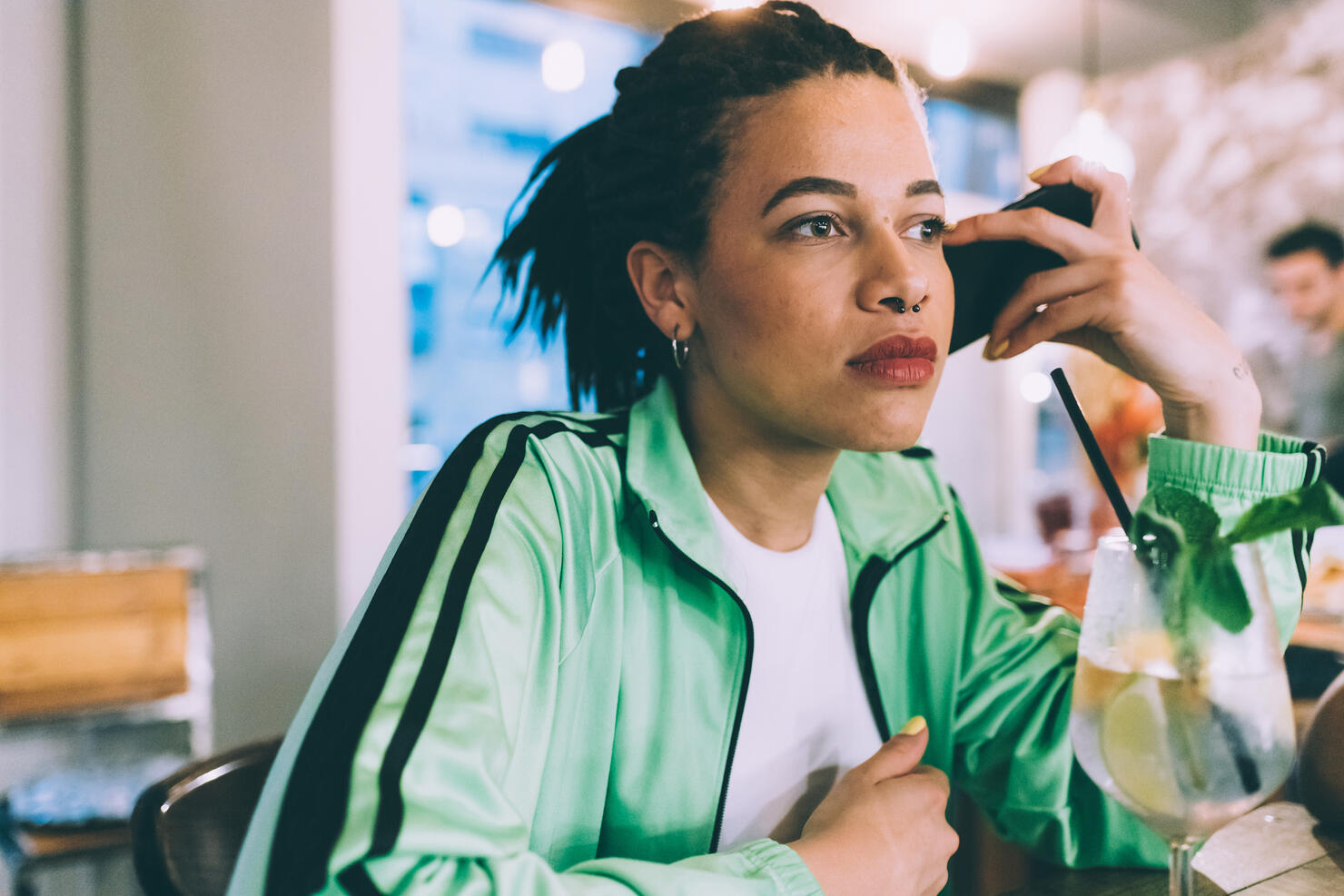 Woman listening to message on mobile while having drink in bar