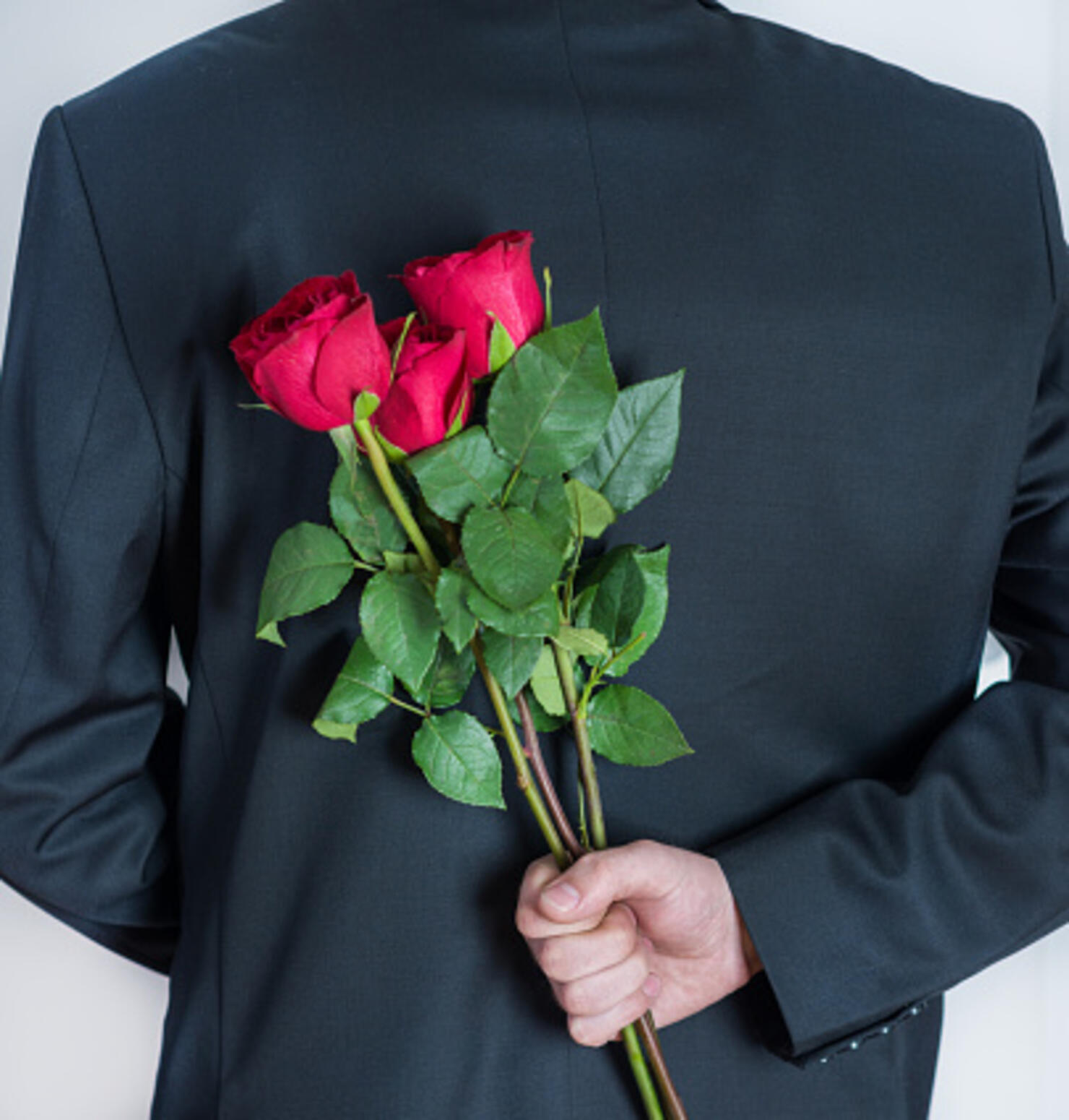 Elegant man holding red rose flowers in hand behind his back