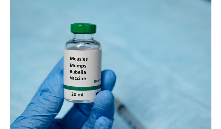 Measles, mumps and rubella vaccine holding in hand with injection syringe at the background