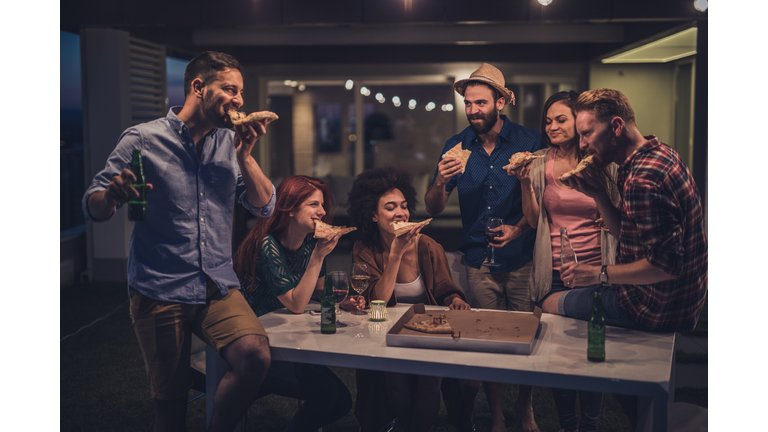 Young happy people eating pizza during the night on a terrace.