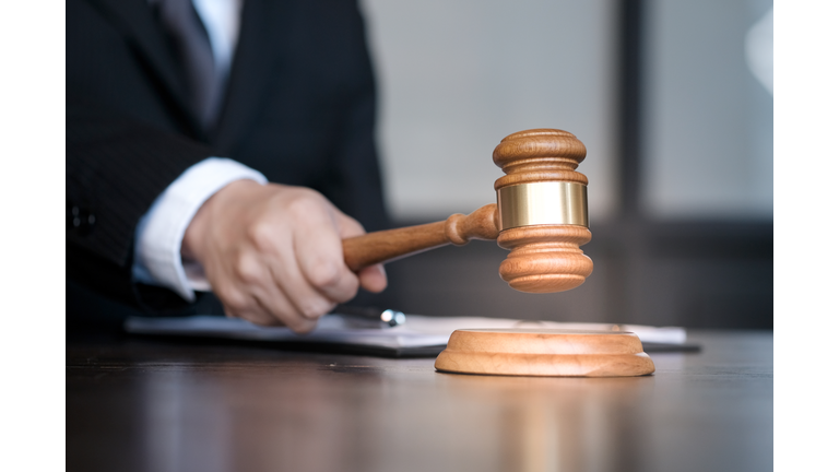 Midsection Of Male Judge Holding Gavel At Desk In Courthouse