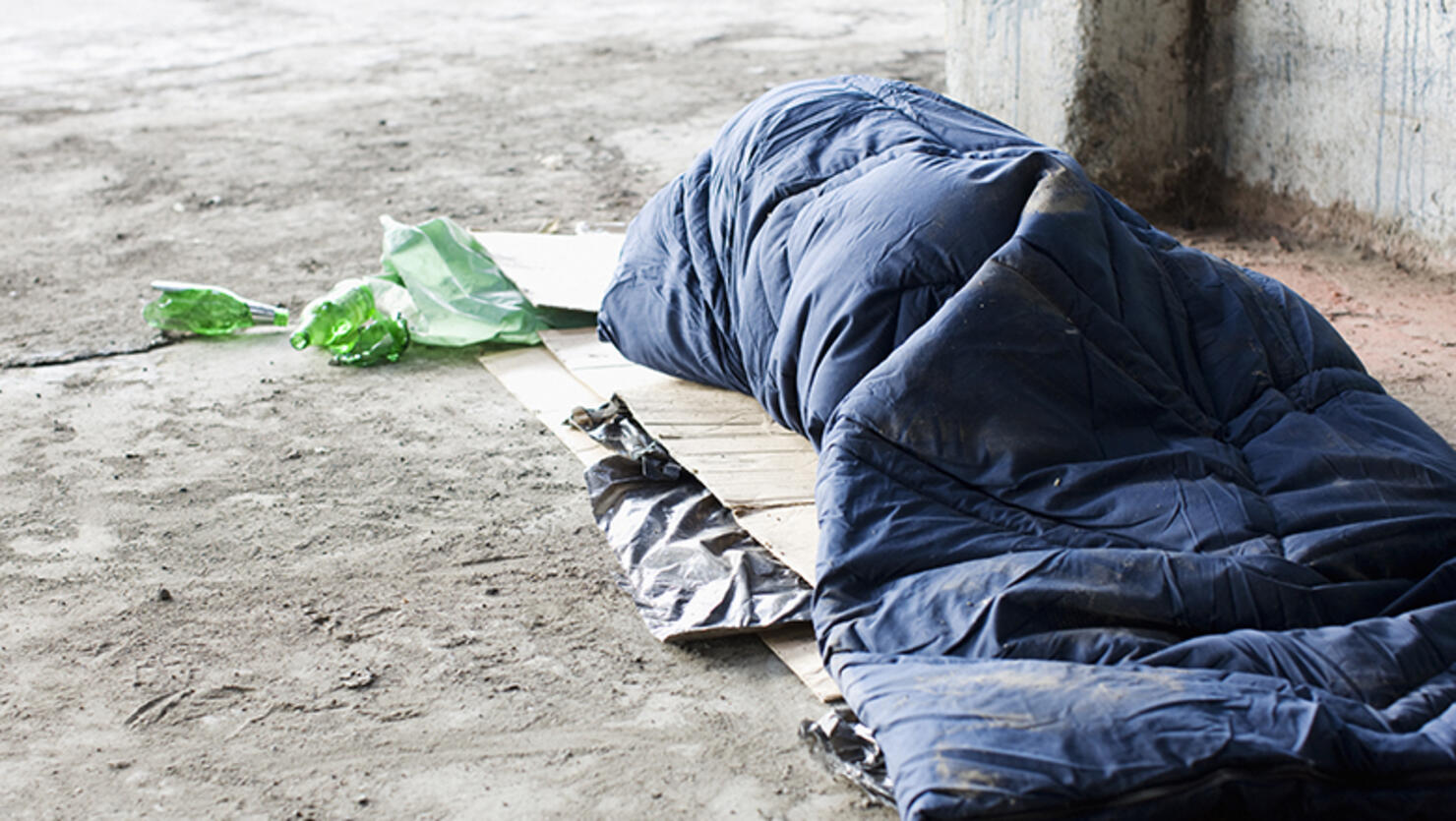 Homeless man sleeping in sleeping bag on cardboard