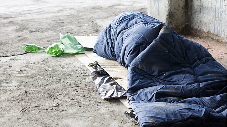 Homeless man sleeping in sleeping bag on cardboard
