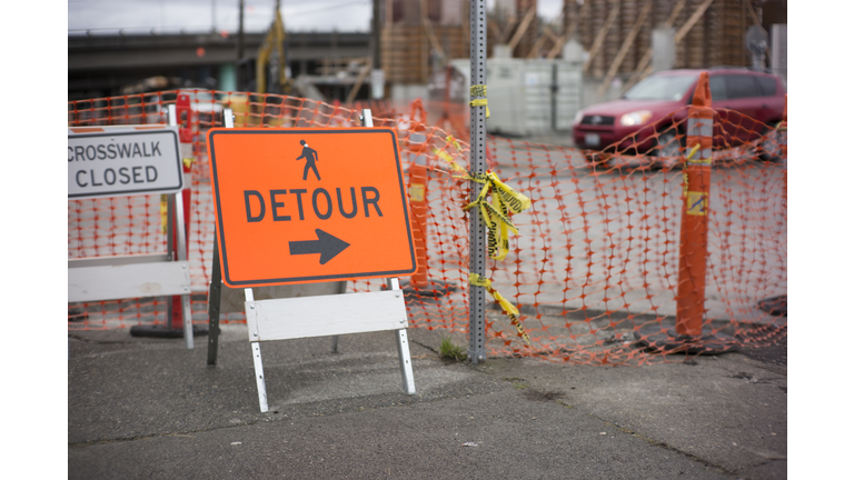 Detour sign on city sidewalk outside a construction site