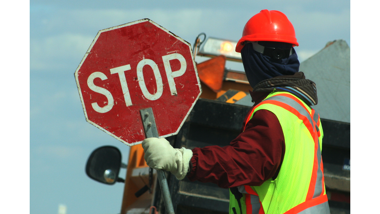 Side View Of Male Worker Holding Stop Sign Against Vehicle On Road