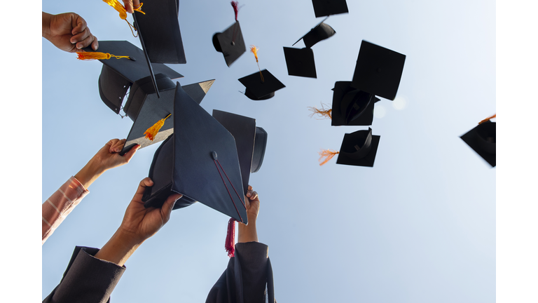 Cropped Hands Of People Throwing Mortarboards Against Clear Sky