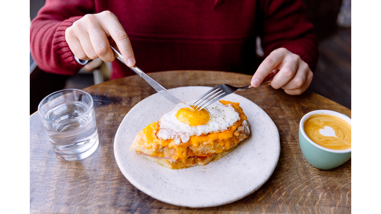 Man eating Croque Madame sandwich with cheese and fried egg