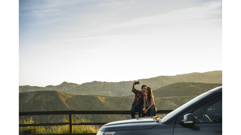 Couple taking selfie while sitting on fence in countryside