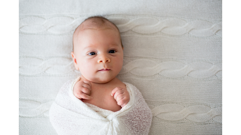 Newborn baby boy, wrapped in knitted wrap looking curiously at camera