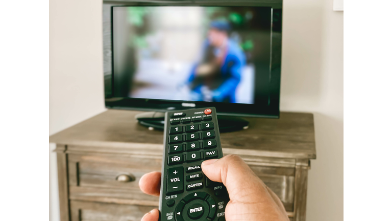 Close-Up View of Hand Pointing Remote Control at TV