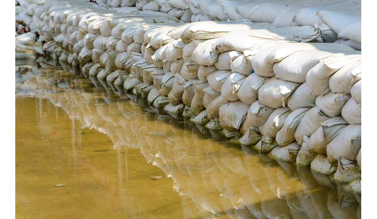 White sandbags for flood defense and it's reflection brown water