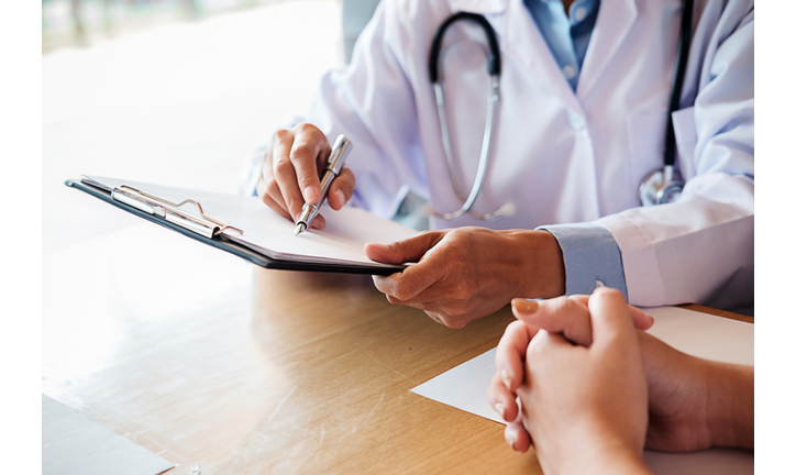 Midsection Of Doctor With Clipboard Discussing With Patient On Table