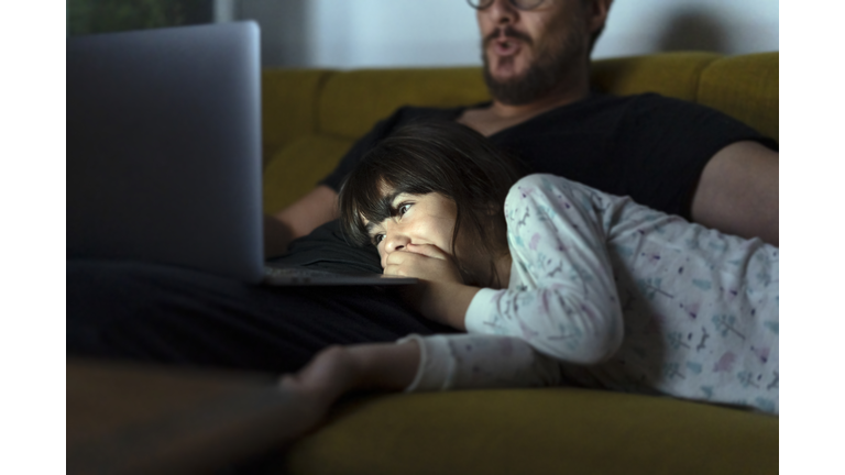 Happy daughter and father looking at laptop on couch at night