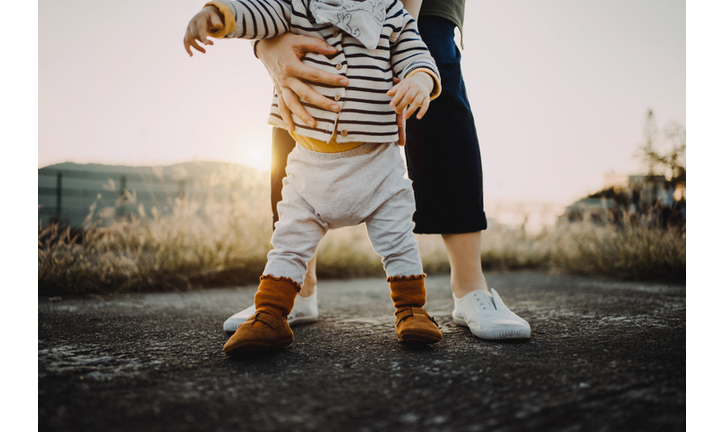 Mother holding baby daughter's body helping her to take her first step in life