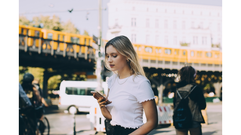 Young woman using mobile phone while walking by street in city