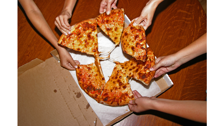 People grabbing slices of pizza, overhead view