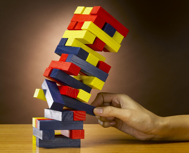 Female hand removing building block, causing tower of blocks to collapse